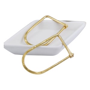 May include: A pair of gold-toned hammered metal hoop earrings. The earrings are open and have a rectangular shape.