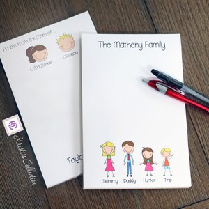 May include: Two white notepad sets with personalized family names and stick figure drawings. The first notepad says "A note from the Mom of..." with stick figure drawings of a girl named Madeleine and a boy named Logan. The second notepad says "The Matheny Family" with stick figure drawings of a family of five: Mommy, Daddy, Hunter, and Trip.