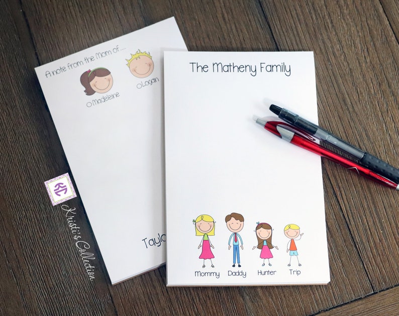 May include: Two white notepad sets with personalized family names and stick figure drawings. The first notepad says "A note from the Mom of..." with stick figure drawings of a girl named Madeleine and a boy named Logan. The second notepad says "The Matheny Family" with stick figure drawings of a family of five: Mommy, Daddy, Hunter, and Trip.