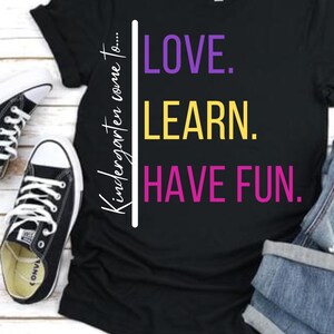 May include: Black t-shirt with the text "Kindergarten come to... LOVE. LEARN. HAVE FUN." in purple, yellow, and pink lettering.