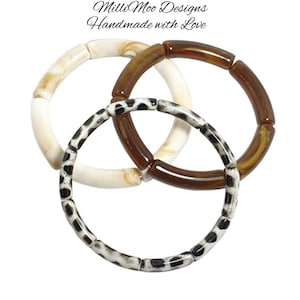 May include: Three interlocking bracelets in cream, brown, and black and white spotted patterns. The bracelets are made of cylindrical beads. The image includes the text "Milli Moo Designs Handmade with Love."