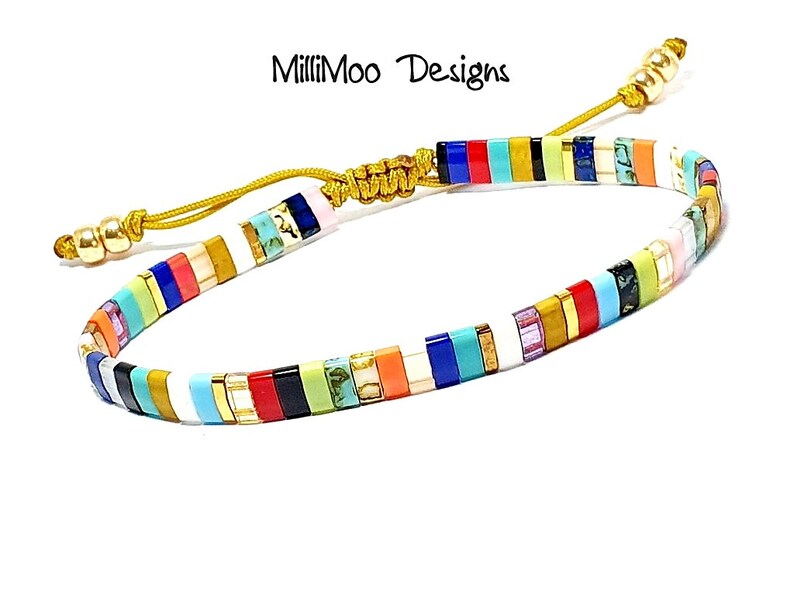 May include: Multicolored beaded bracelet with a gold cord and a sliding knot closure. The beads are arranged in a striped pattern with white, red, orange, yellow, green, blue, turquoise, and purple beads.