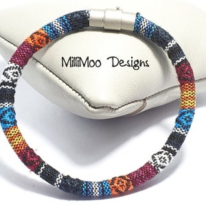 May include: A colourful woven bracelet with a magnetic clasp. The bracelet is made of black, white, blue, orange and red thread. The bracelet is on a white background.