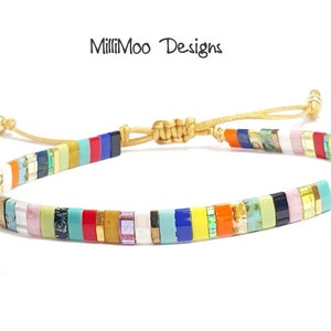 May include: Multicolored beaded bracelet with a gold cord closure. The beads are small and rectangular, and they are arranged in a repeating pattern of different colors. The bracelet is tied with a sliding knot, allowing for a custom fit.