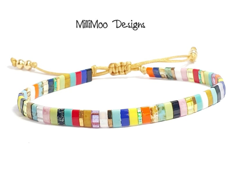 May include: Multicolored beaded bracelet with a gold cord closure. The beads are small and rectangular, and they are arranged in a repeating pattern of different colors. The bracelet is tied with a sliding knot, allowing for a custom fit.
