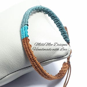 May include: A macrame bracelet in blue and brown. The bracelet has a woven design and a sliding knot fastening. The text "Milli Moo Designs Handmade with Love" is visible on the background.