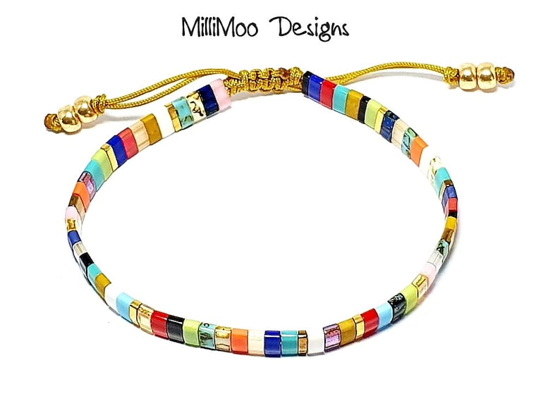 May include: Multicolored beaded bracelet with a gold cord and toggle clasp. The beads are arranged in a striped pattern with colors including white, red, blue, green, yellow, orange, and pink.