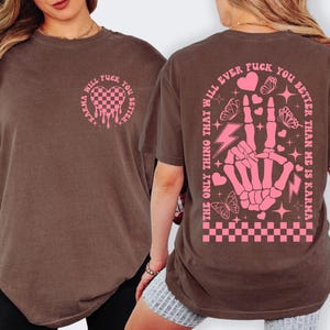 May include: Brown t-shirt with pink graphic text and design. The front features a heart-shaped design with the text "Karma Will Fuck You Better". The back has a skeleton hand making a peace sign with the text "The only thing that will ever fuck you better than me is karma".
