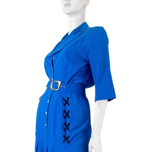 May include: A blue dress with a white collar and a black belt. The dress has a button-up front and a pleated skirt. There is a black lace-up detail on the side of the dress.