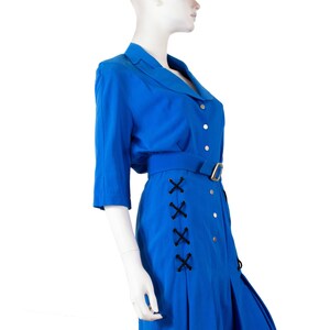 May include: A royal blue dress with a collared neckline, button closure, and a black criss-cross detail on the side. The dress has a belt and a pleated skirt.