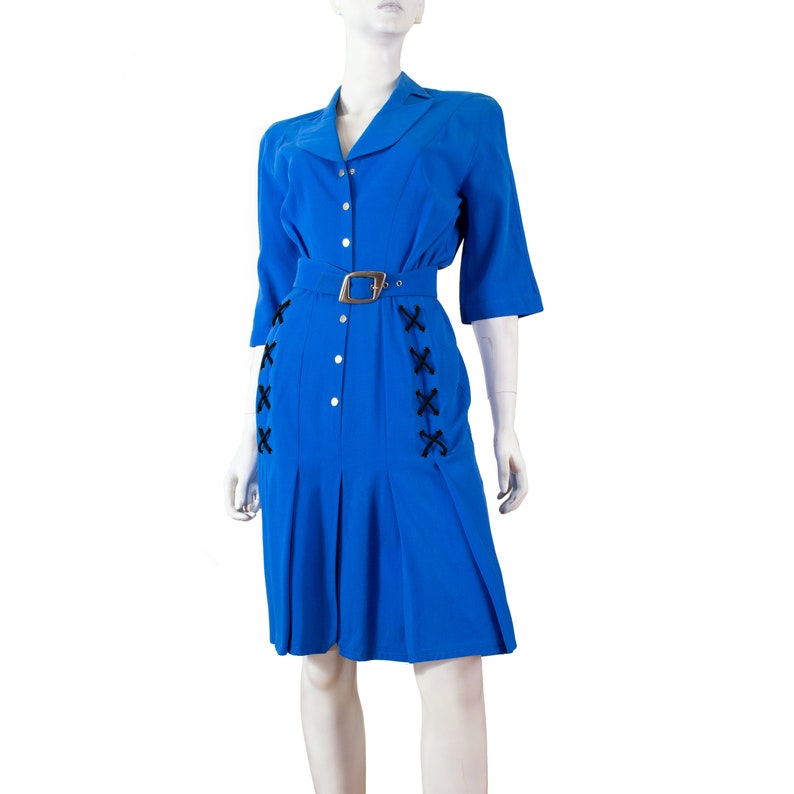 May include: A blue dress with a white collar and black lacing detail on the sides. The dress has a belt and a button-up front.