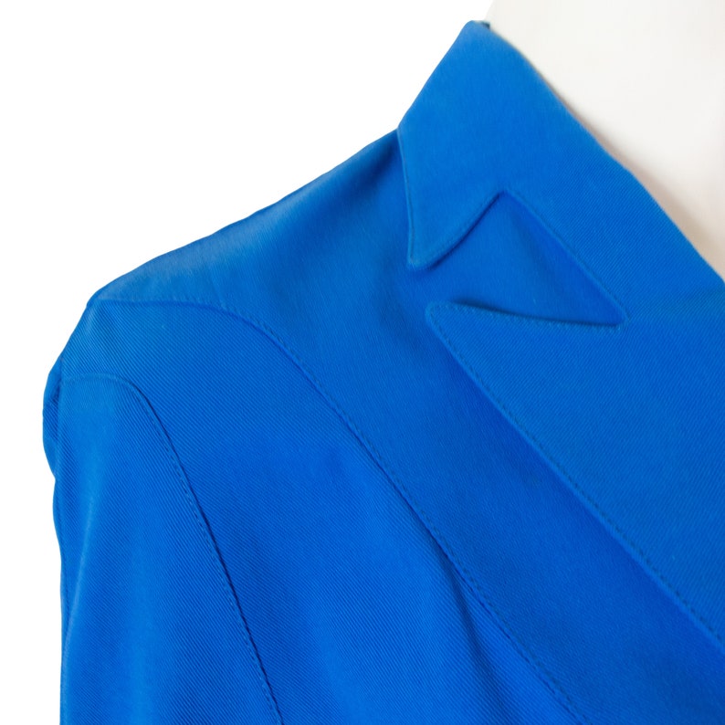May include: Close-up of a bright blue blazer with a notched collar. The fabric has a subtle texture.