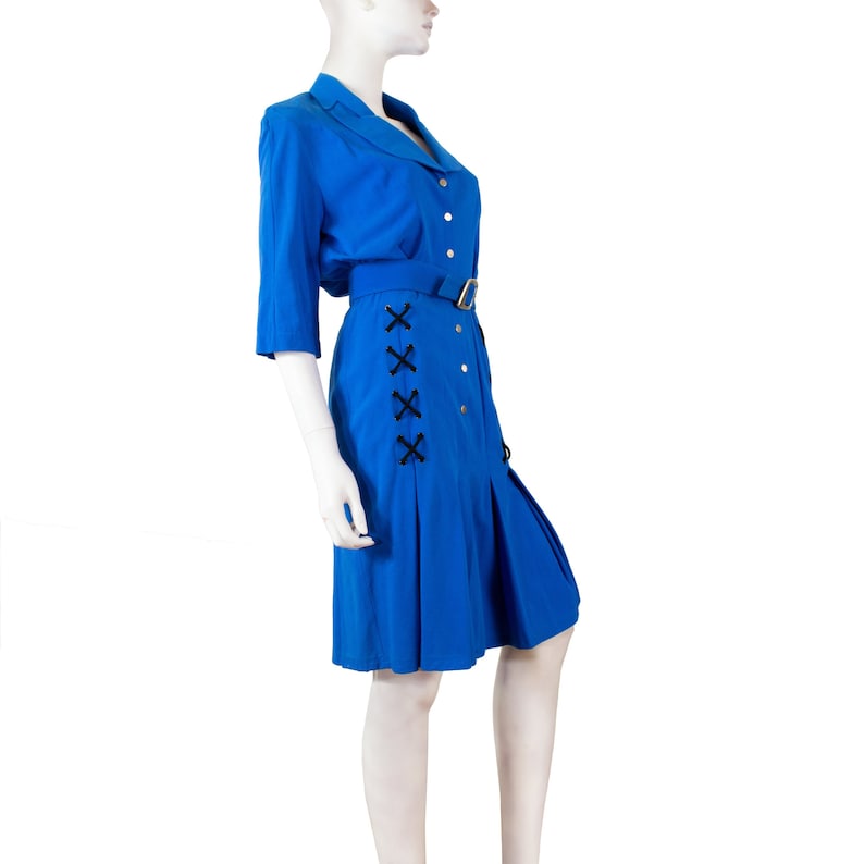 May include: A royal blue dress with a collared neckline, button closure, and a black criss-cross detail on the side. The dress has a belt and a pleated skirt.