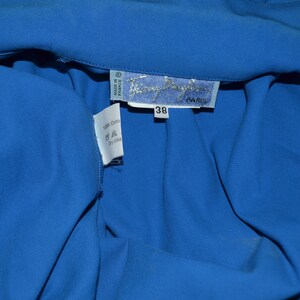 May include: A blue cotton shirt with a white tag that says "Made in France" and "100% Cotton" with a dry clean symbol. The tag also has the brand name "Thierry Mugler" and "Paris" printed on it. The shirt has a size tag that says "38".