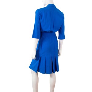 May include: A royal blue dress with a collared neckline and a belt. The dress has a pleated skirt and three-quarter sleeves.