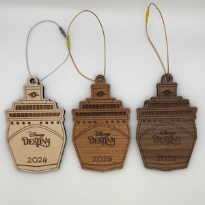 May include: Three wooden Disney Destiny cruise ship ornaments. Each ornament is a different shade of brown, with the ship's name and the year 2026 engraved on the front. They have a loop for hanging.