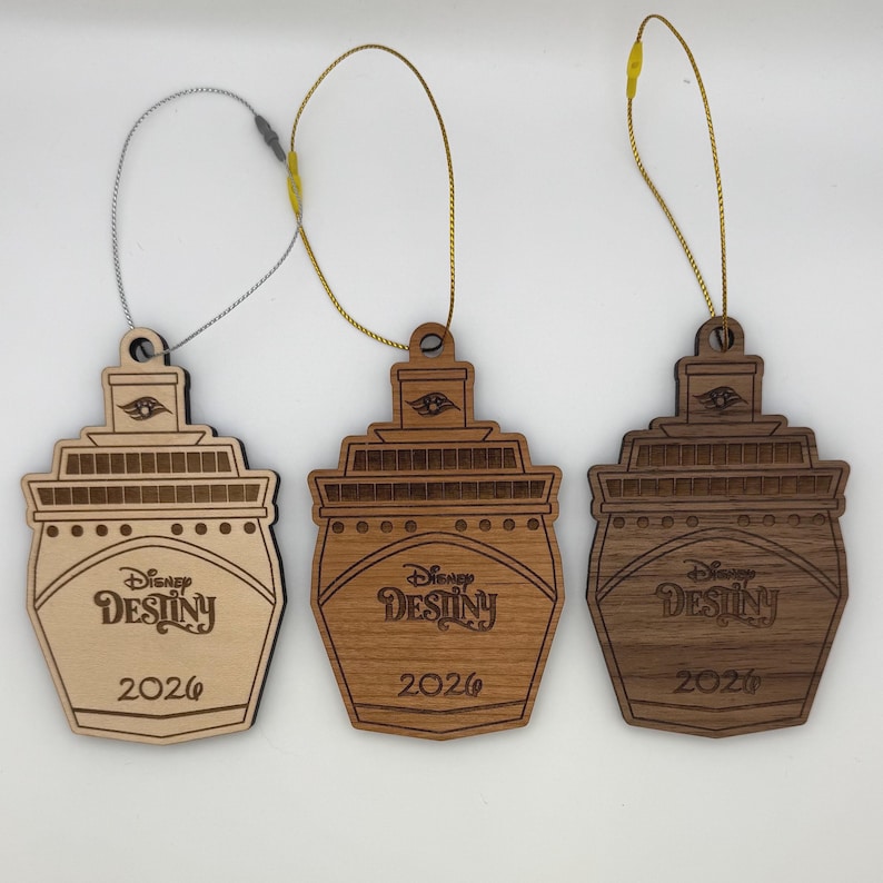 May include: Three wooden Disney Destiny cruise ship ornaments. Each ornament is a different shade of brown, with the ship's name and the year 2026 engraved on the front. They have a loop for hanging.