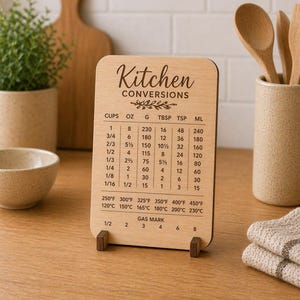 May include: A wooden kitchen conversion chart displaying "Kitchen Conversions". It details measurements in cups, ounces, grams, tablespoons, teaspoons, and millilitres. Temperature conversions are also included on the chart.
