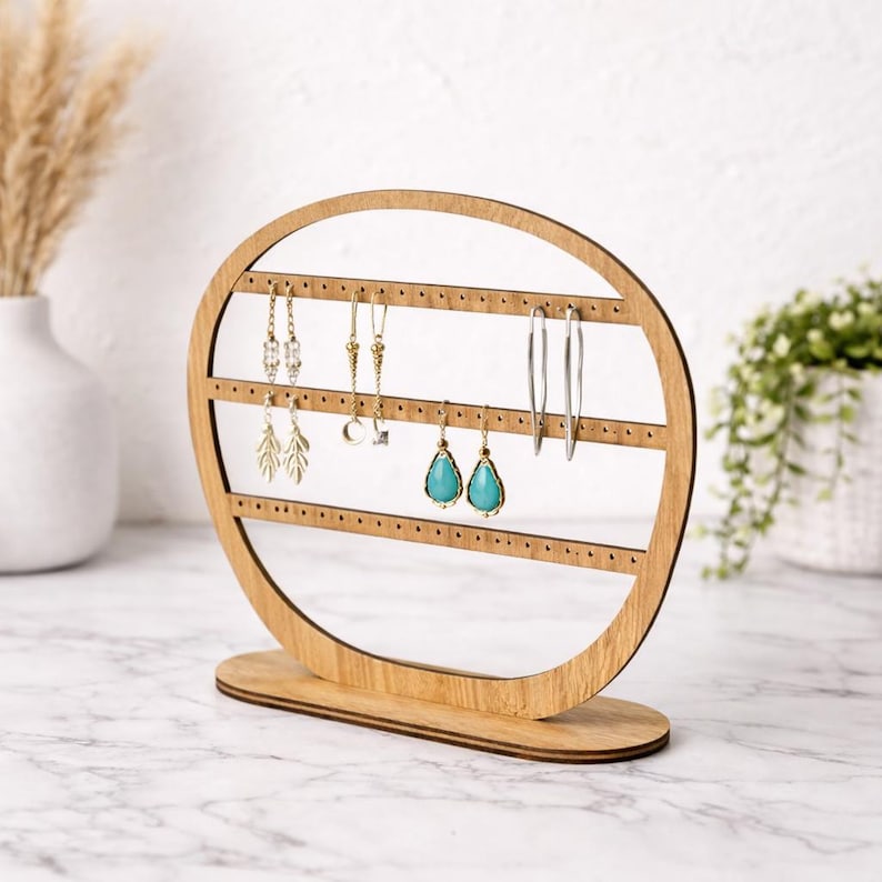 May include: A wooden earring display stand with a light brown finish. The stand has an oval shape with multiple horizontal rows of small holes to hold earrings. Several pairs of earrings, including silver hoops and turquoise teardrop earrings, are displayed.