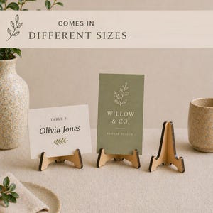 May include: Wooden table card holders with cards that read "Olivia Jones" and "Willow & Co. Floral Design." The cards are displayed on a neutral surface with a vase and a plate with a napkin. The text "COMES IN DIFFERENT SIZES" is also visible.