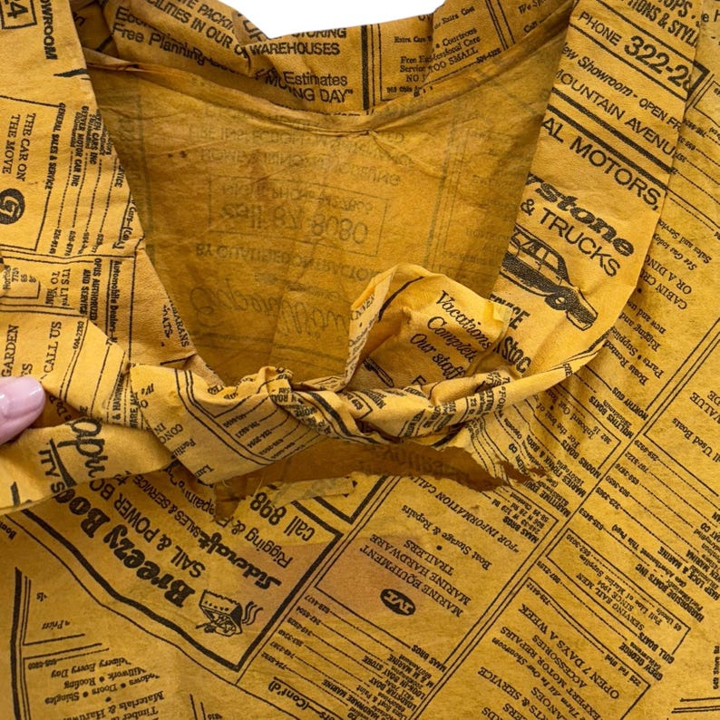 Może przedstawiać: Pognieciona ż&oacute;łta papierowa torba z nadrukiem gazety. Torba jest otwarta, odsłaniając wnętrze. Nadruk gazety zawiera r&oacute;żne reklamy i tekst. Torba jest prawdopodobnie używana do pakowania lub przenoszenia przedmiot&oacute;w.