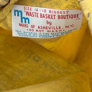 Może przedstawiać: Zbliżenie na metkę odzieżową w stylu vintage. Etykieta jest biała z niebieskim i czerwonym tekstem i zawiera tekst "WASTE BASKET BOUTIQUE" firmy MARS OF ASHEVILLE, N.C. Etykieta zawiera r&oacute;wnież informacje o rozmiarze i ostrzeżenie dotyczące łatwopalności.