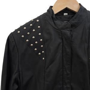 以下が含まれることがあります： 肩に銀色のスタッズが付いた黒い革のジャケット。 ジャケットはスタンドカラーとジッパー開閉式です。 木製のハンガーにかかっています。