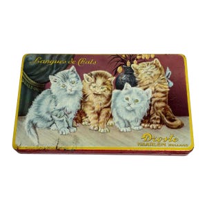 May include: Vintage rectangular tin featuring an illustration of four fluffy kittens in shades of gray, brown, and orange. The tin has the text "Langues de Chats" and "Droste HAARLEM HOLLAND" in gold lettering against a red background.