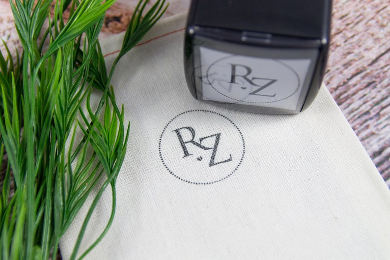 May include: A black self-inking stamp with the initials "RZ" in a circle. The stamp is on a white fabric pouch with the same initials stamped in the center.