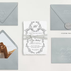May include: A set of wedding invitations with a light blue envelope, a white invitation with a floral wreath design, and a white envelope with a photo of a couple kissing on the beach.