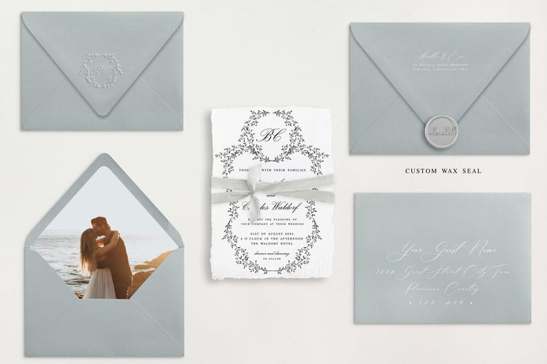 May include: A set of wedding invitations with a light blue envelope, a white invitation with a floral wreath design, and a white envelope with a photo of a couple kissing on the beach.