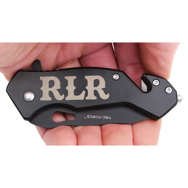 May include: Black folding pocket knife with a silver engraved inscription that reads "RLR" and a silver safety feature. The knife has a black handle and a silver blade.
