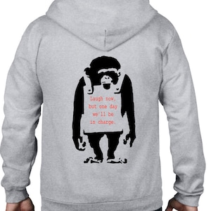 Puede incluir: Una sudadera con capucha gris con una imagen en blanco y negro de un mono que lleva un cartel que dice "Laugh now, but one day we'll be in charge."