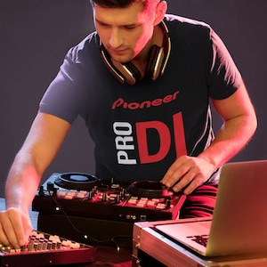 May include: A person wearing a navy blue t-shirt with the text "Pioneer Pro DJ" in white and red letters. The person is using a black DJ mixer with a laptop computer.