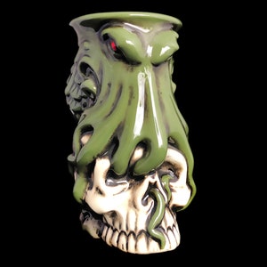 May include: Green ceramic mug with a skull and octopus design. The octopus has a red eye and is wrapped around the skull.