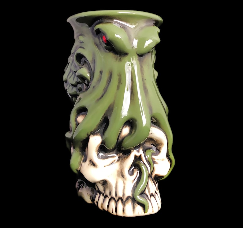 May include: Green ceramic mug with a skull and octopus design. The octopus has a red eye and is wrapped around the skull.