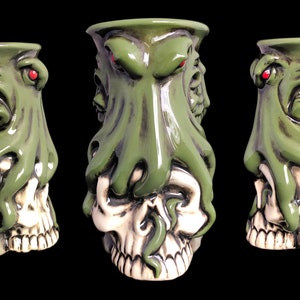 May include: Green ceramic mug shaped like a skull with a green octopus wrapped around it. The octopus has red eyes and tentacles.