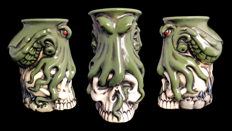 May include: Green ceramic mug shaped like a skull with a green octopus wrapped around it. The octopus has red eyes and tentacles.