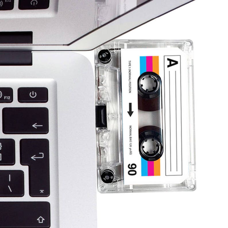 May include: A clear plastic cassette tape with a white label. The label has the text "TYPE 1 (NORMAL) POSITION", "NORMAL BIAS 120 &mu;s EQ", and "90". The cassette tape is next to a silver laptop computer.