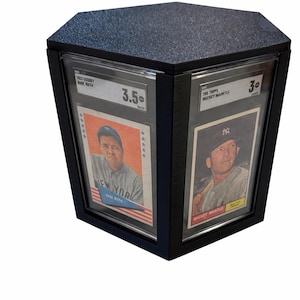 Puede incluir: Expositor negro con tapa texturizada, que muestra dos tarjetas de b&eacute;isbol vintage. Una tarjeta presenta a Babe Ruth, la otra a Mickey Mantle. Las tarjetas est&aacute;n calificadas y encapsuladas, con calificaciones visibles.