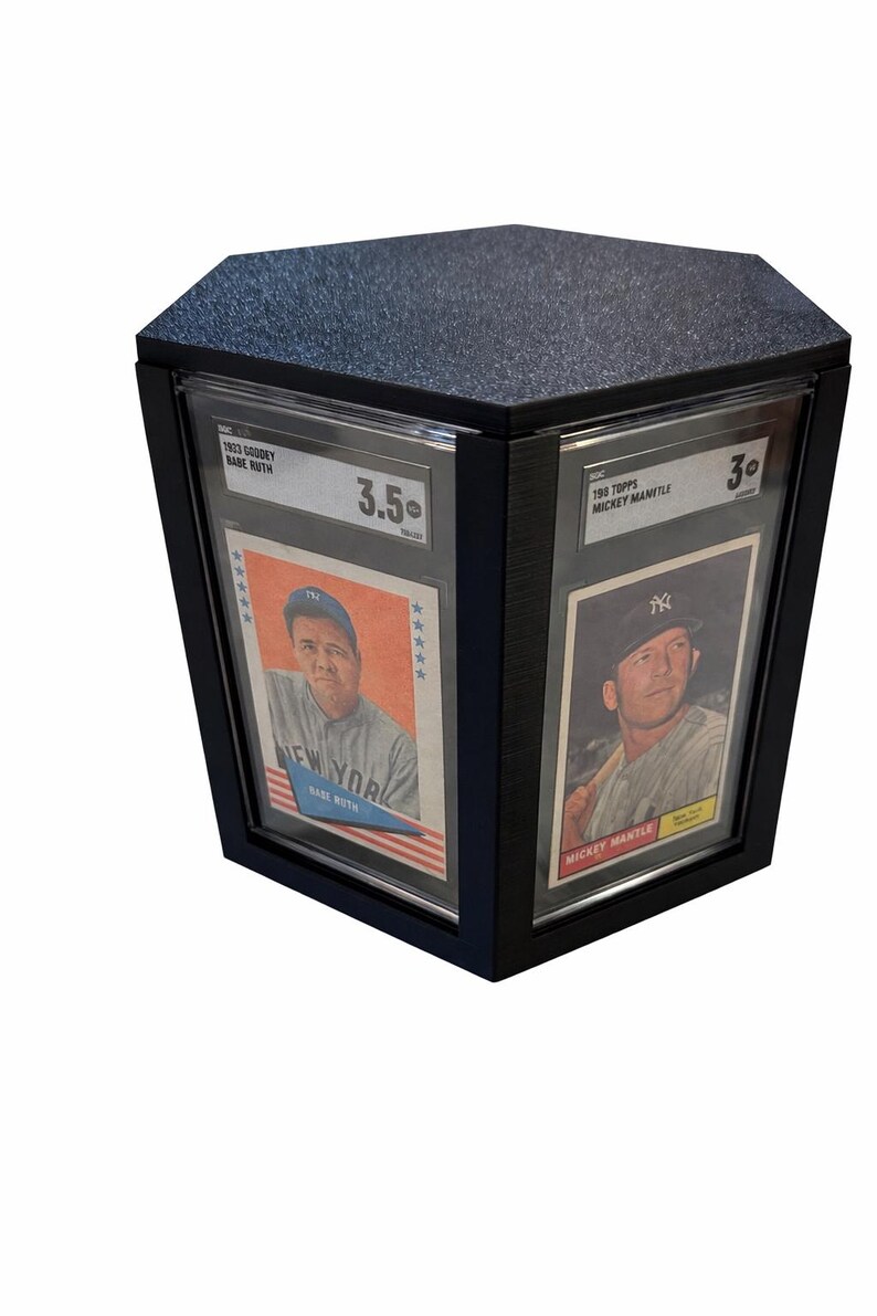 Puede incluir: Vitrina negra con tapa texturizada, que muestra dos tarjetas de b&eacute;isbol vintage. Una tarjeta presenta a Babe Ruth, la otra a Mickey Mantle. Las tarjetas est&aacute;n calificadas con 3.5 y 3.0, respectivamente.