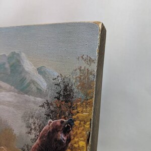 May include: A close-up of a wooden wall art piece featuring a brown bear with its mouth open, roaring. The bear is standing in a forest setting with mountains in the background. The art piece has a rustic, distressed look.