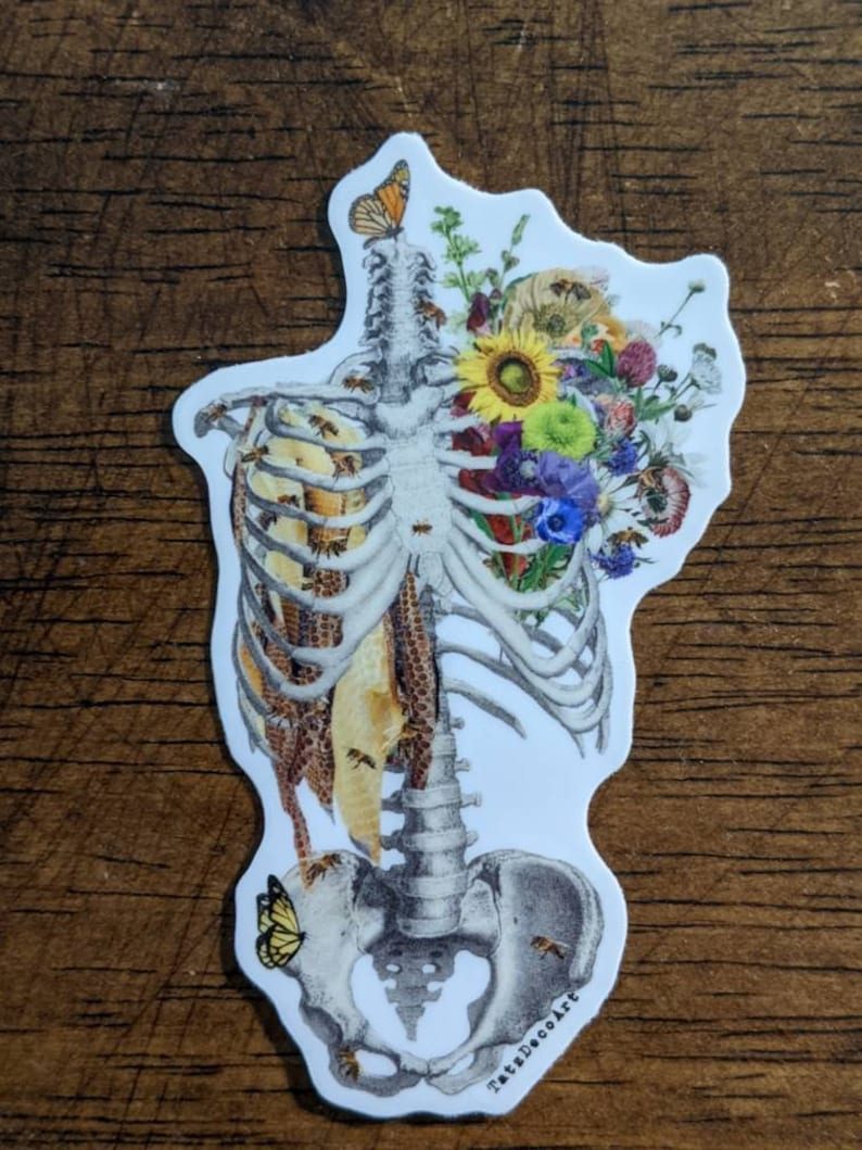 May include: A white sticker with a detailed illustration of a human skeleton with a bouquet of flowers and honeycomb in the chest cavity. The flowers are in shades of yellow, purple, and blue. There are bees and butterflies flying around the skeleton. The sticker has the text "TattoDecoArt" at the bottom.