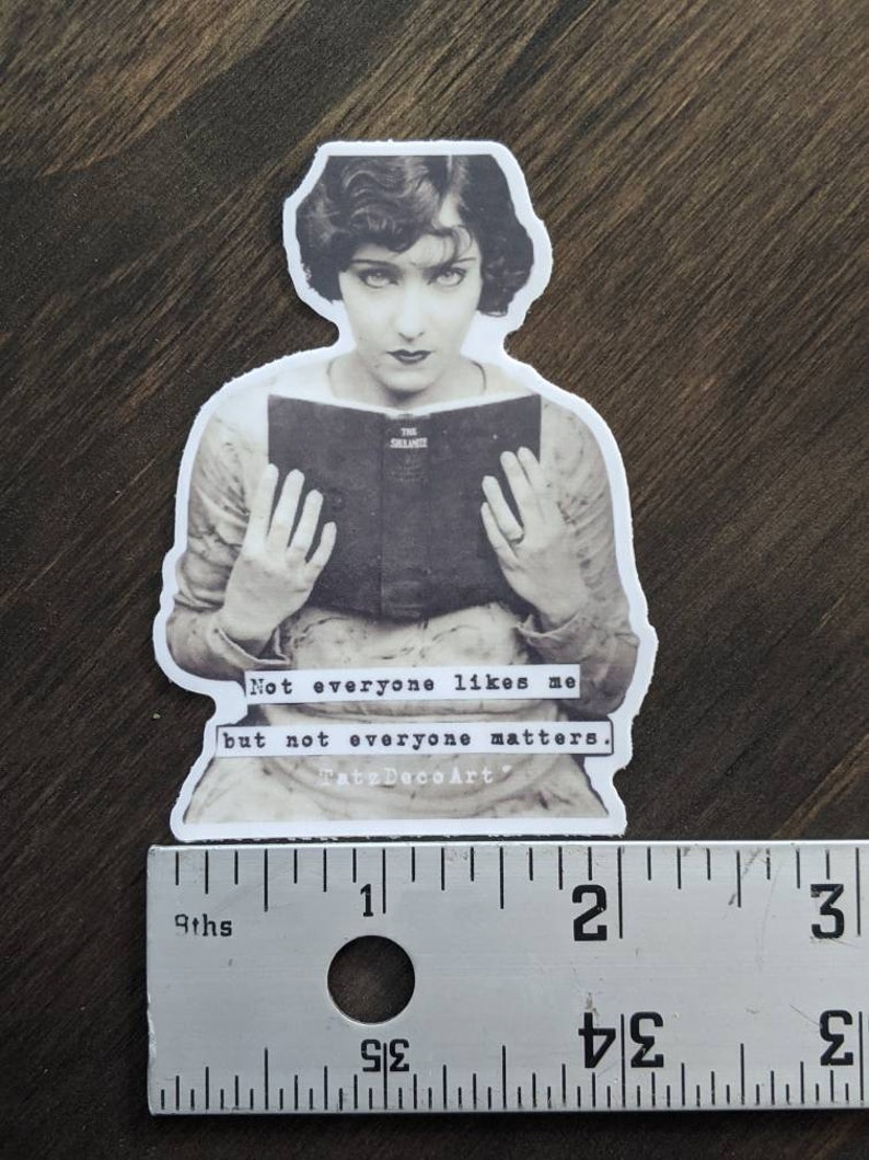 Pu&ograve; includere: Immagine in bianco e nero di una donna che legge un libro. Il libro &egrave; aperto e la donna lo tiene con entrambe le mani. Il testo sul libro recita "The Silence". L'immagine &egrave; un adesivo con il testo "Not everyone likes me but not everyone matters. Tatz Deco Art" sotto l'immagine.