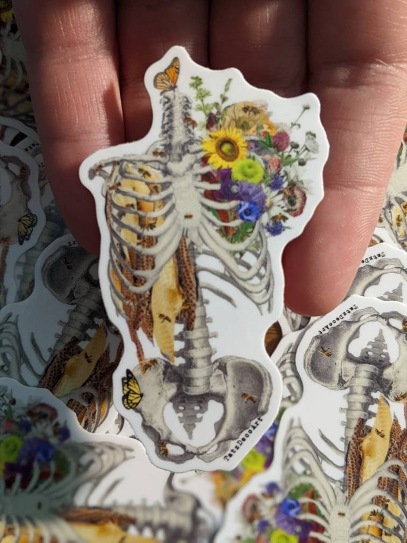 May include: A white sticker with a detailed illustration of a human skeleton with a honeycomb pattern inside the rib cage. The skeleton is adorned with a bouquet of colorful flowers, including sunflowers, bluebells, and butterflies.