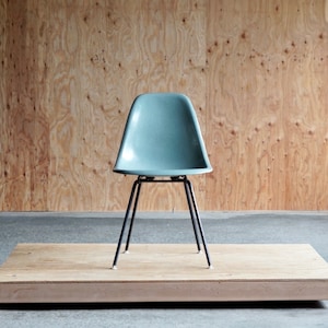 May include: A light blue fiberglass chair with black metal legs sits on a wooden platform. The chair is a classic mid-century modern design.