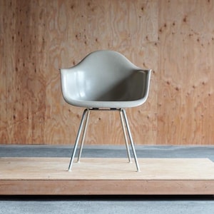 May include: A light gray molded plastic chair with a metal frame and four legs. The chair is sitting on a wooden platform.