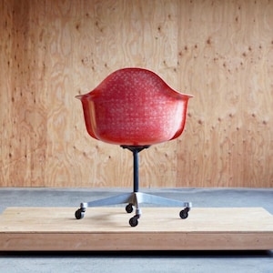 May include: A red office chair with a white speckled finish and a silver base with four wheels. The chair is sitting on a wooden platform.