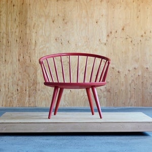 May include: A red wooden chair with a curved back and a slatted design. The chair is sitting on a wooden platform.
