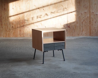 May include: A small wooden side table with two drawers and a shelf. The table has black metal legs and is sitting on a concrete floor.